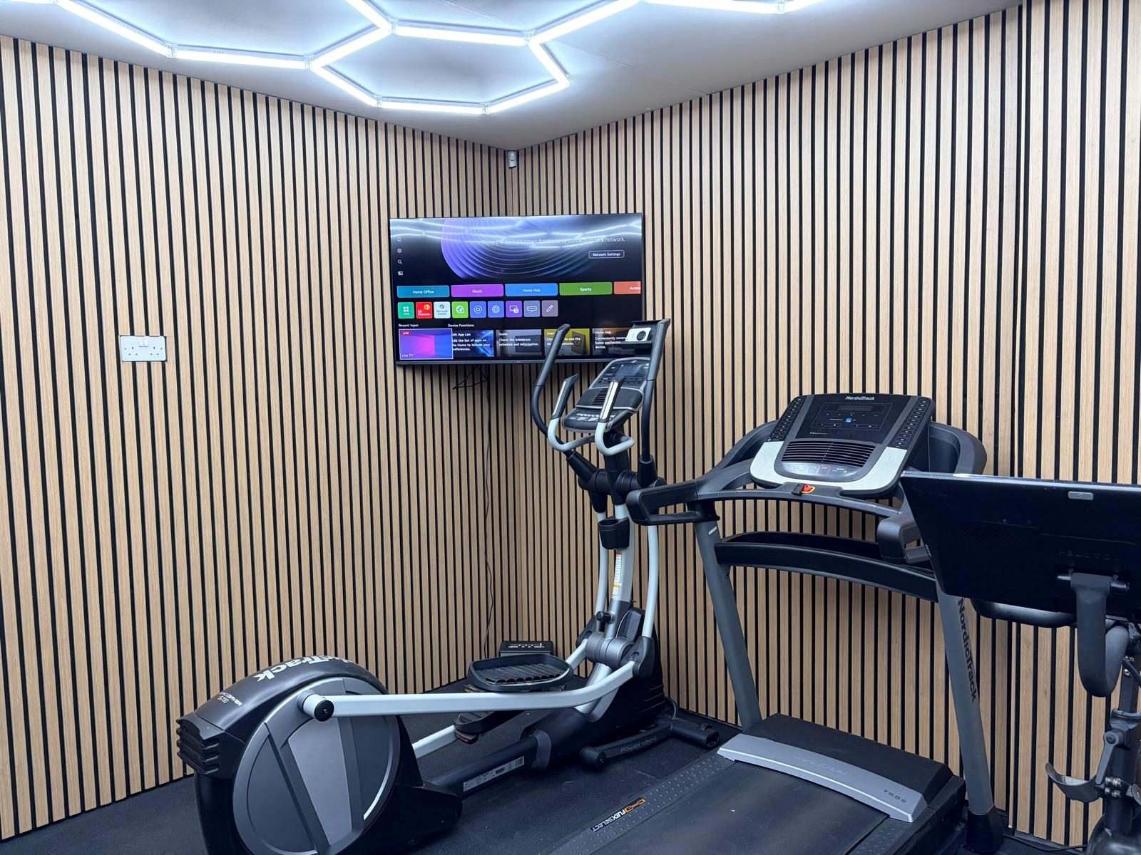 Cross trainer and treadmill facing a wall-mounted TV on vertical wood slat panelling in the Durham conversion