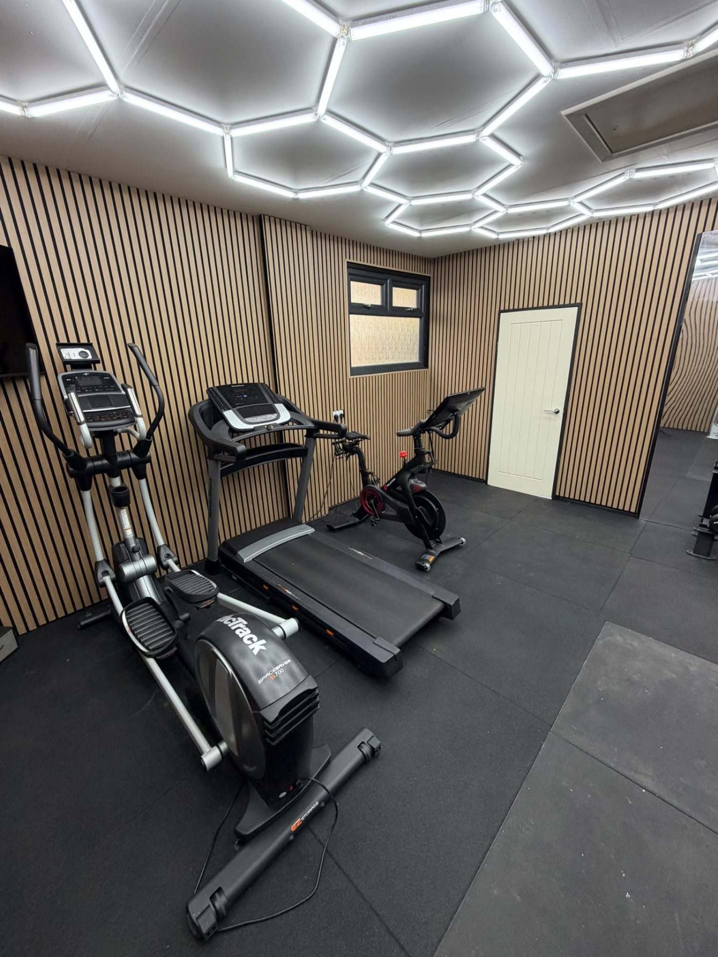 Portrait view of the cardio row with cross trainer, treadmill and exercise bike beside the new window and white internal door
