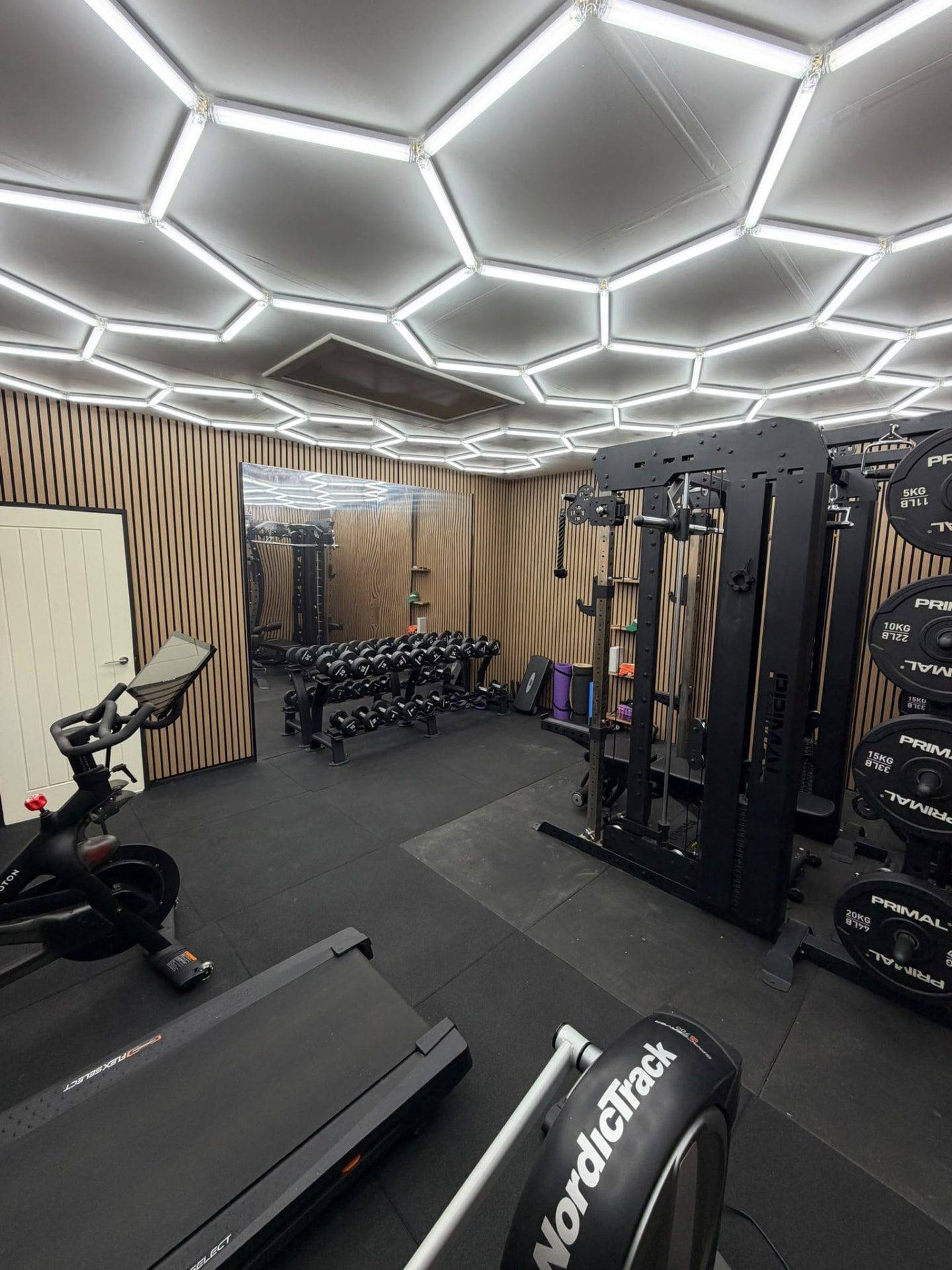 Looking back across the gym towards the mirror wall, dumbbell rack and cage rack, with the treadmill and bike in the foreground