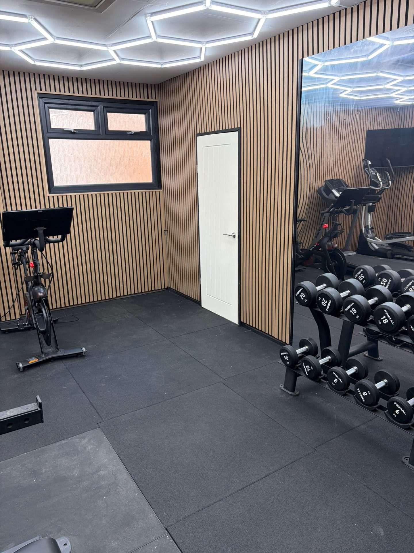 Corner by the new window and internal door with an exercise bike, dumbbell rack and wall mirror on rubber flooring
