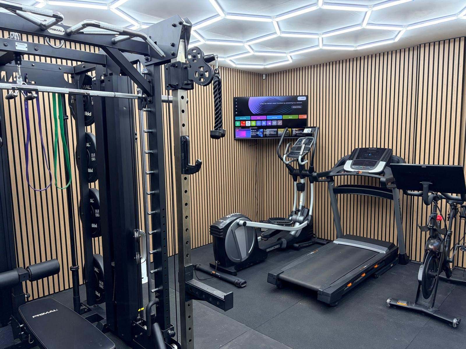 Converted garage gym in Durham with treadmill, cross trainer, spin bike, wall-mounted TV and slat wall panelling
